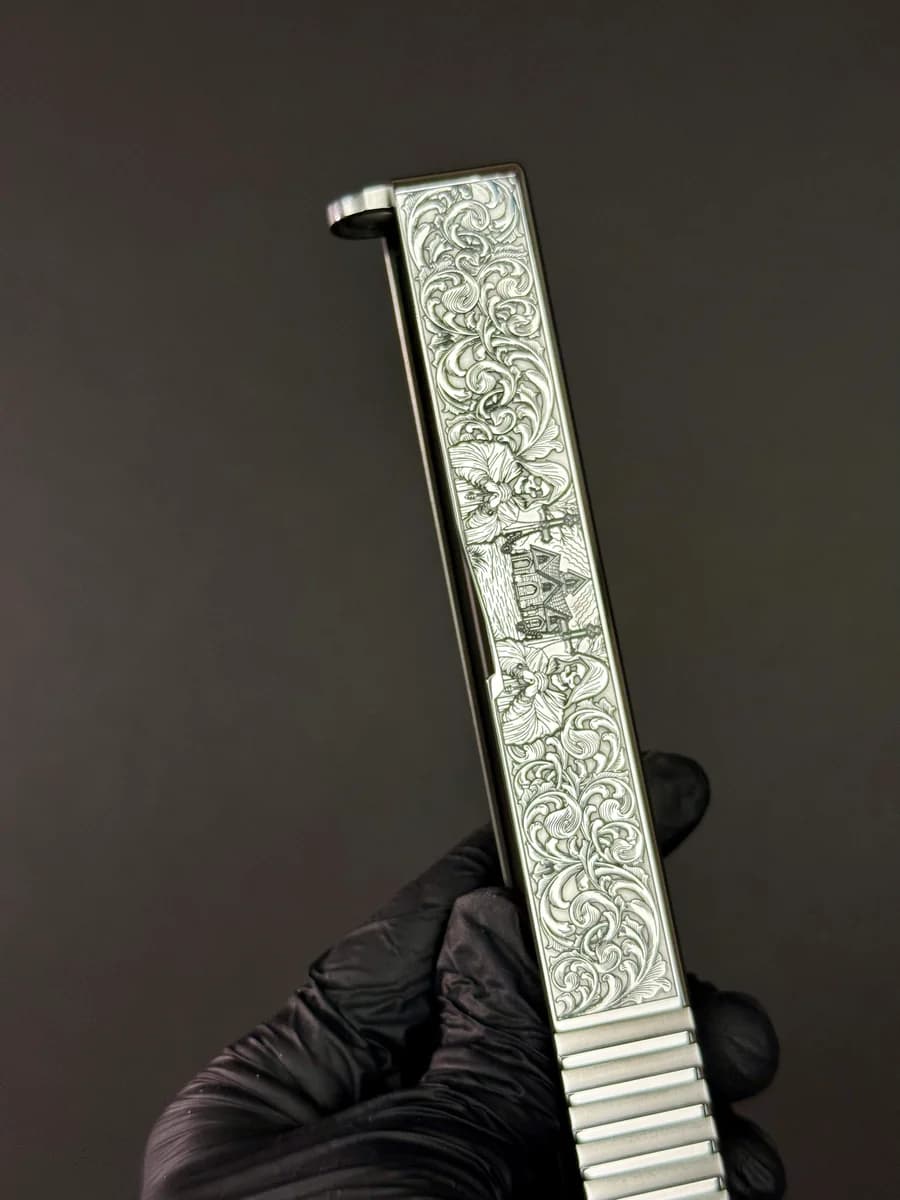 Laser-engraved 1911 pistols with scrollwork and gold inlays on a wooden table
