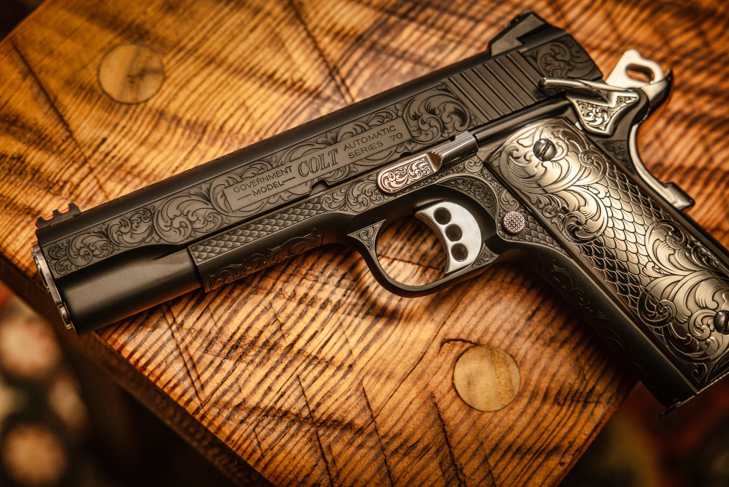 Colt Government Model with full scrollwork engraving on warm wood surface